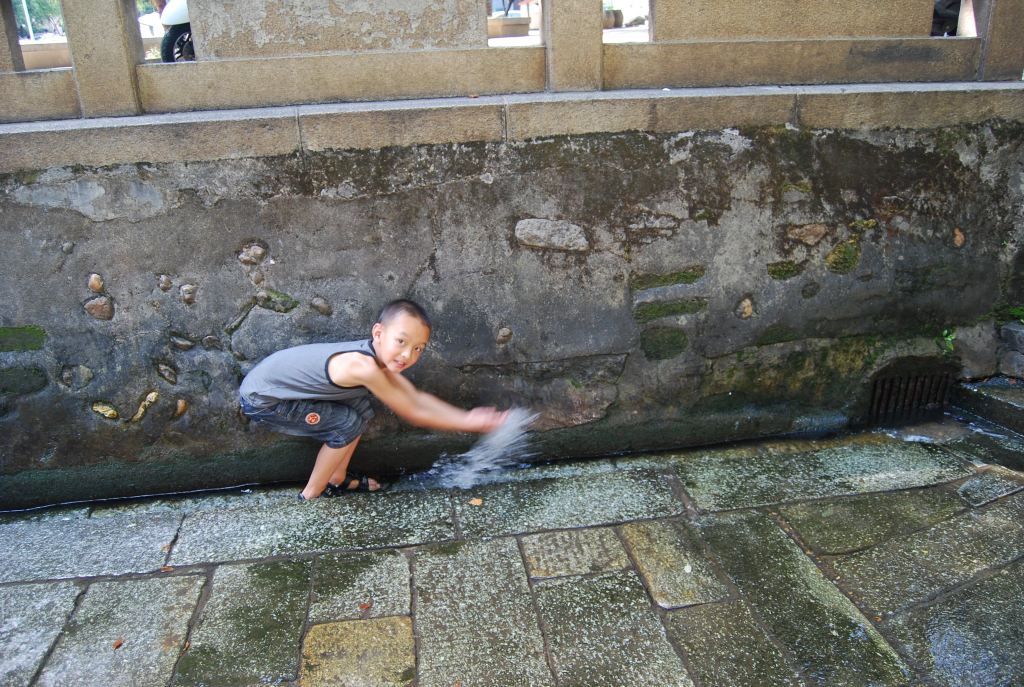 许多孩子欢快地喊叫着,脱下鞋子冲进井旁边的小水沟嬉水.